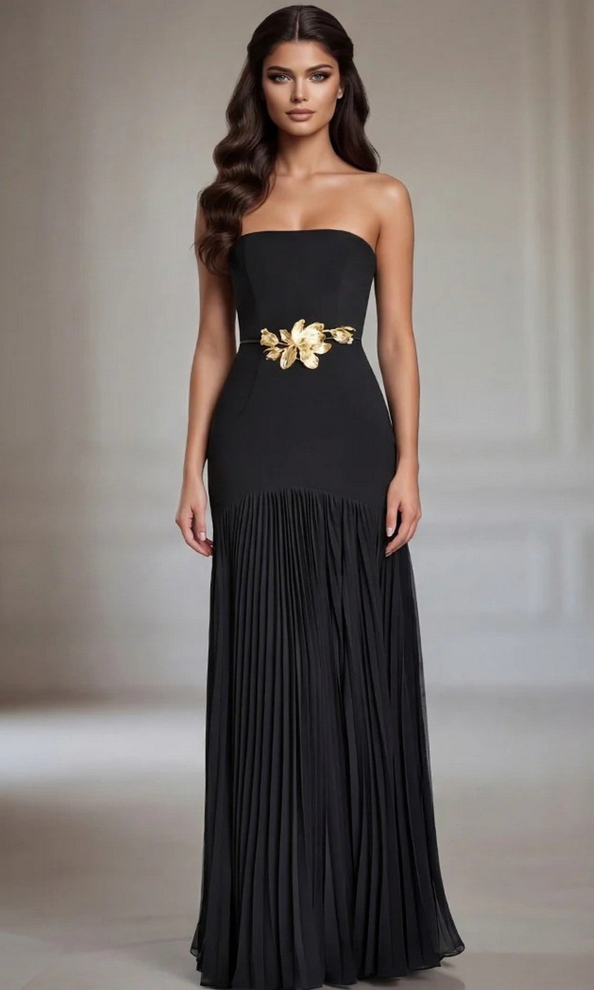 A woman wearing the Long Formal Dress: Jovani 47000—a black, strapless floor-length gown featuring a pleated skirt and an elegant gold floral waist detail—stands indoors against a neutral background.